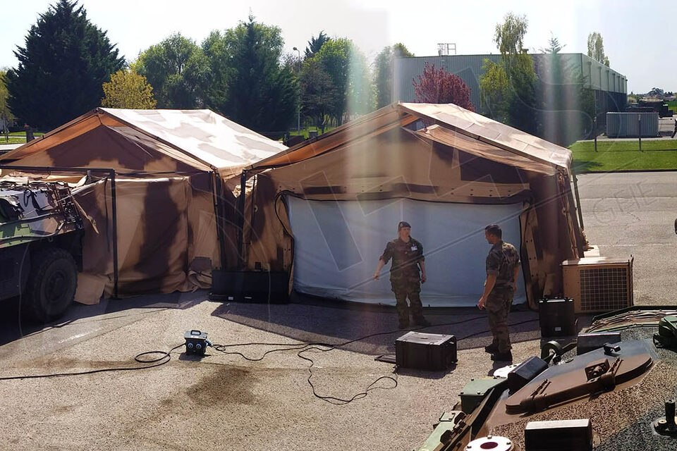 Deux abris I-4S raccordés sur un terrain, véhicule blindé accolé et militaires au travail