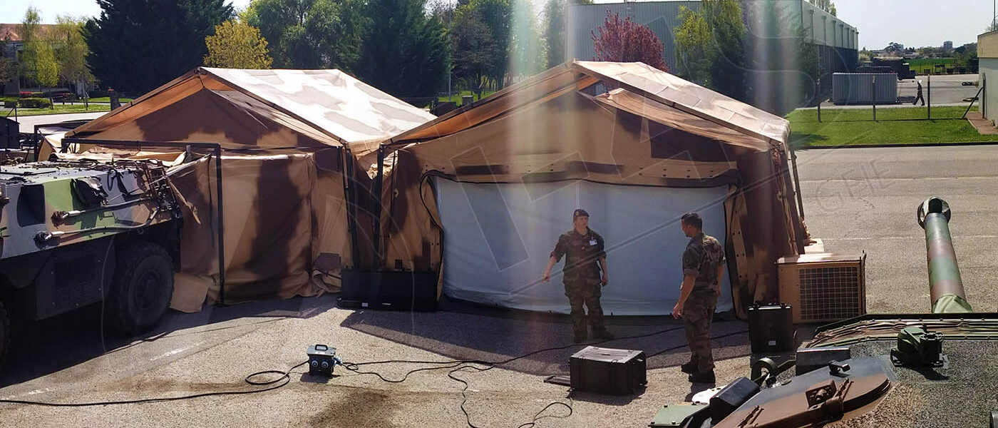 Abris I-4S déployés sur un terrain, véhicule blindé accolé et militaires au travail